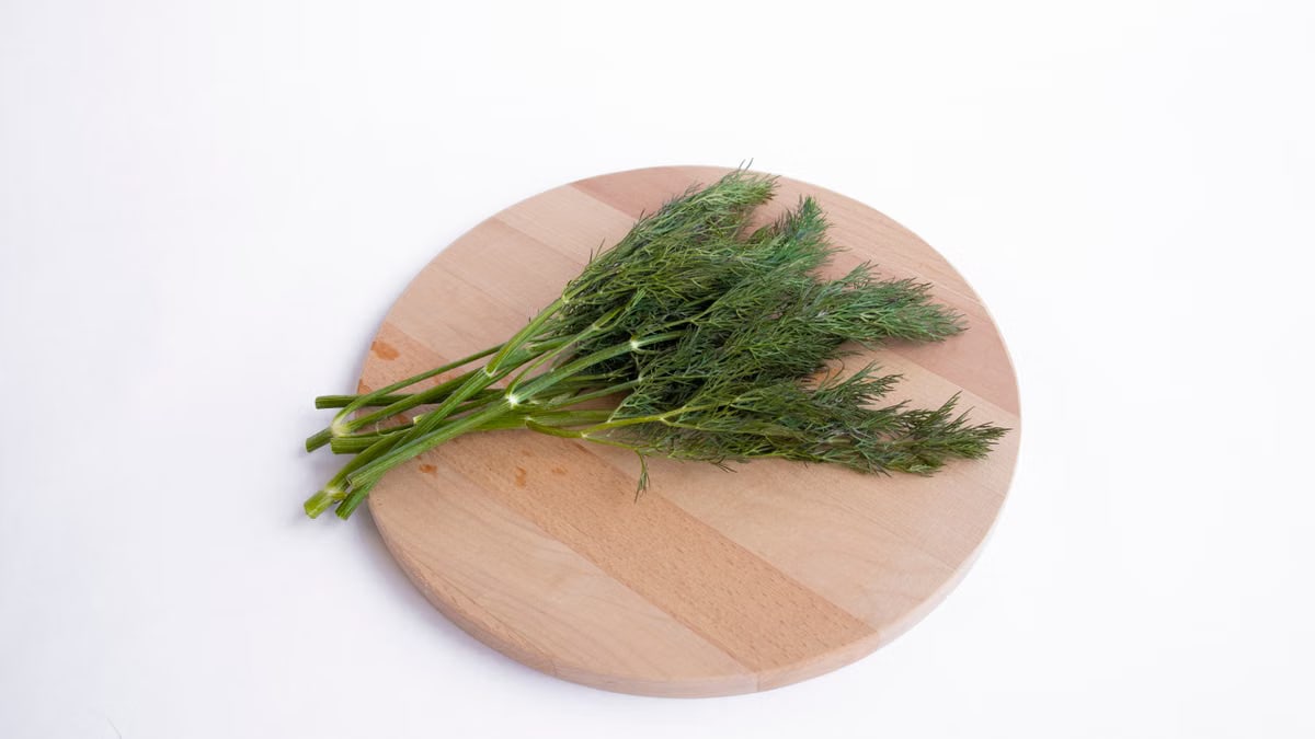 High-quality image of fresh dill sprigs on a wooden cutting board against a white background.